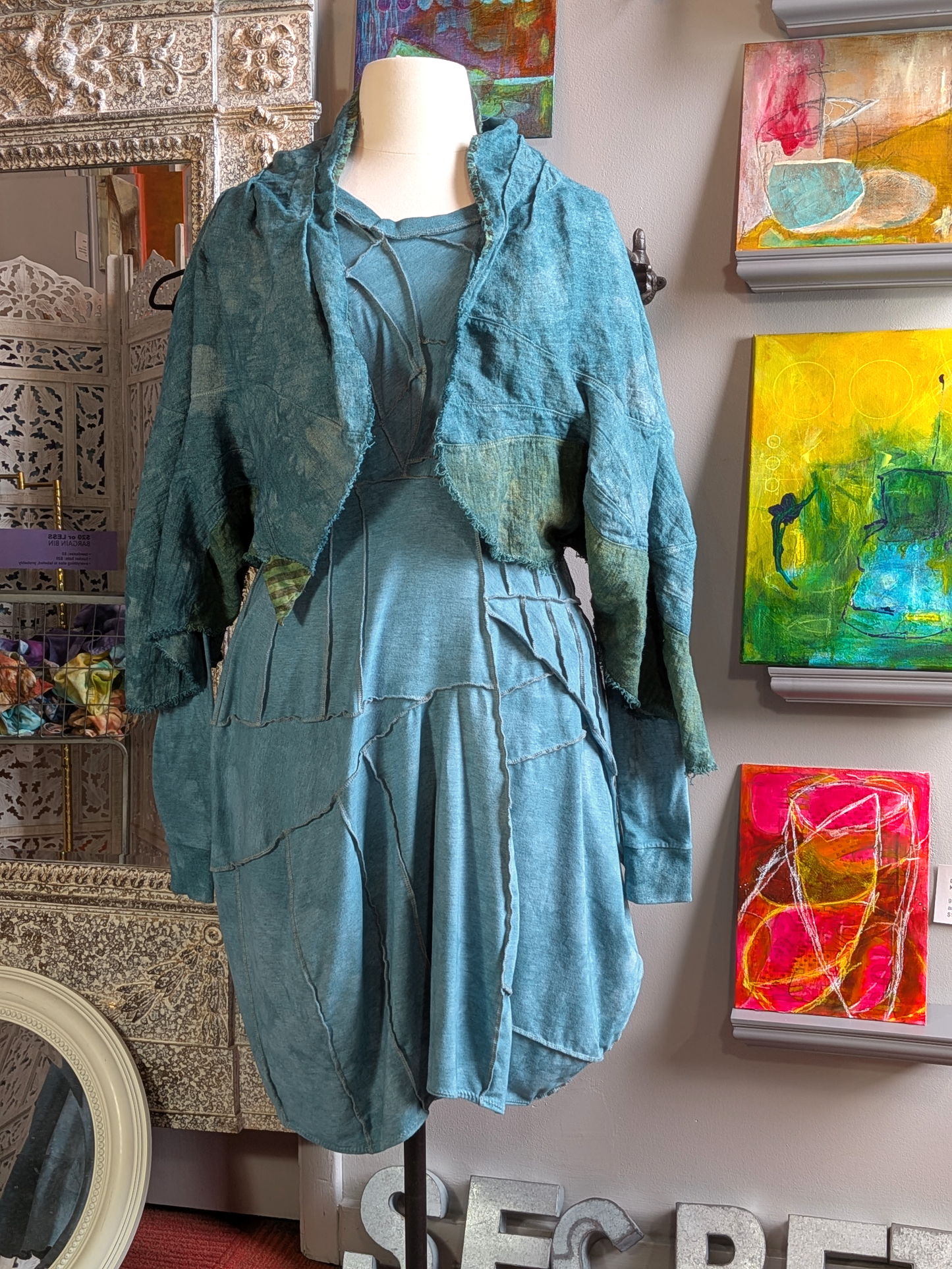 Mannequin wearing a teal outfit with abstract paintings in the background