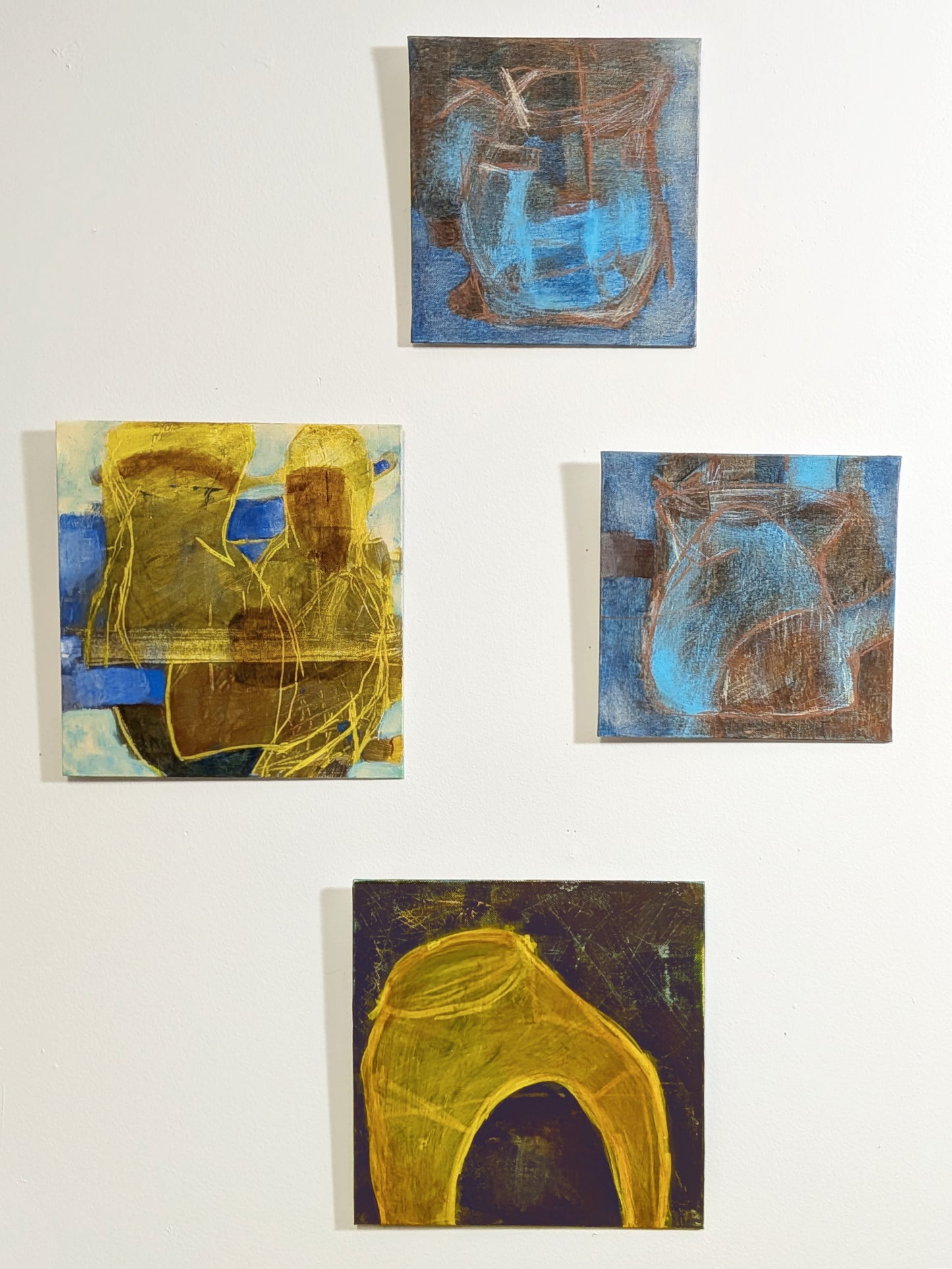 helen carter - Four small abstract paintings arranged on a white wall, featuring blue, yellow, brown, and black tones.