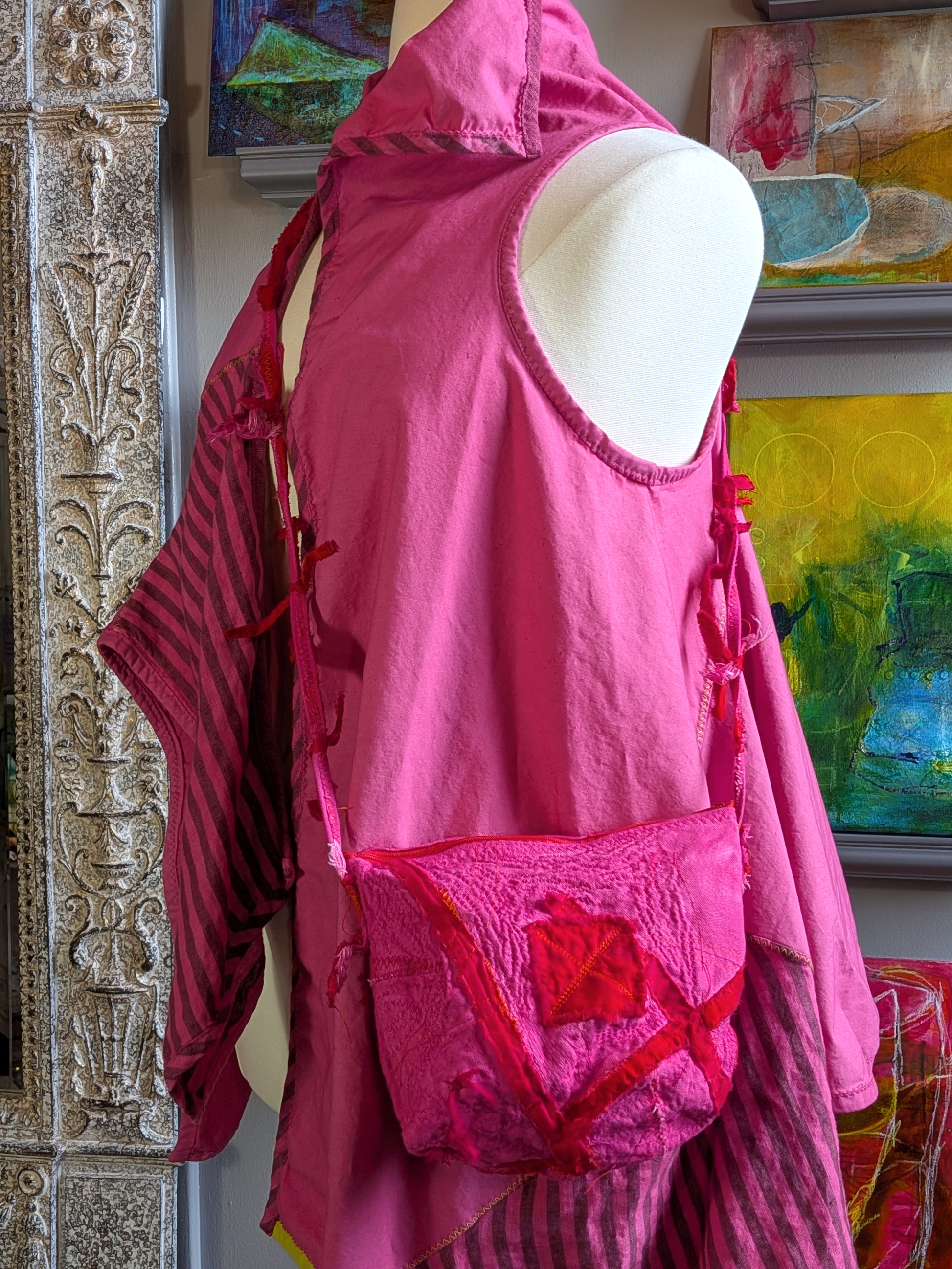 Mannequin wearing a pink outfit with a red bag against a colorful abstract painting.