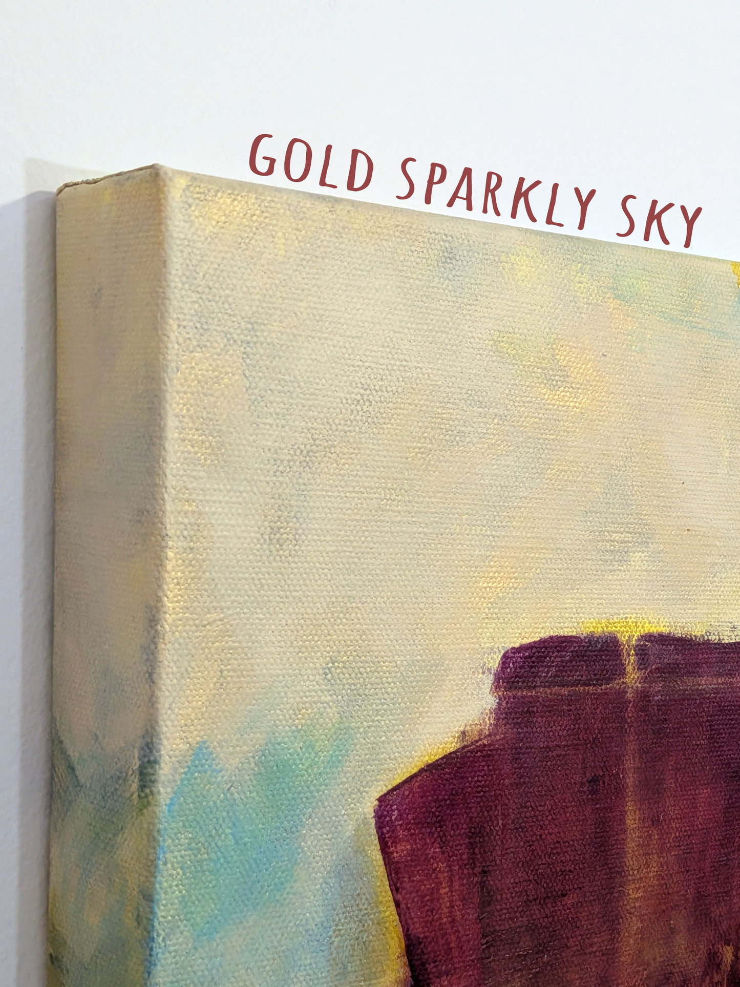 Close-up of a canvas wall art print showing an abstract painted sky with the words 'GOLD SPARKLY SKY' above it. The artwork features a textured cream and yellow sky with hints of blue and a dark burgundy abstract shape at the bottom.