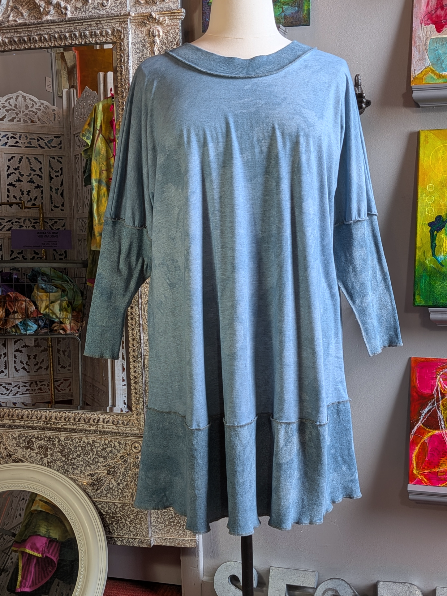Blue dress on a mannequin against a decorative wall with art and mirrors.