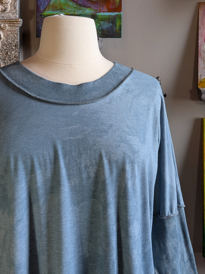 Blue long-sleeve top on a mannequin against a neutral wall with artwork.