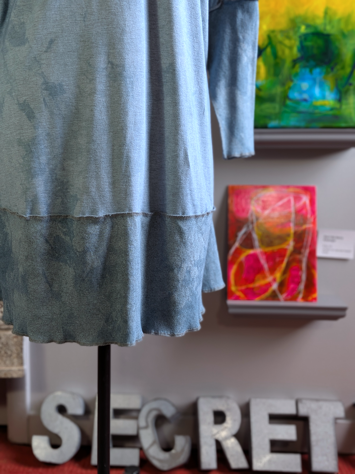 Blue dress on a mannequin with abstract paintings in the background
