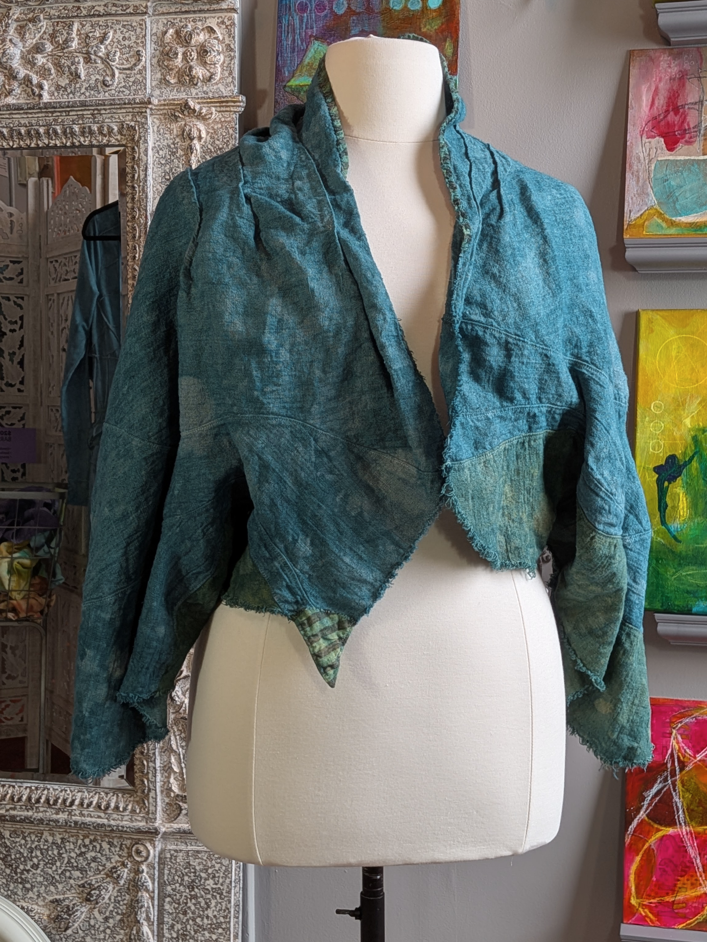 Teal textured jacket on a mannequin against a decorative wall with colorful abstract paintings. - secret lentil