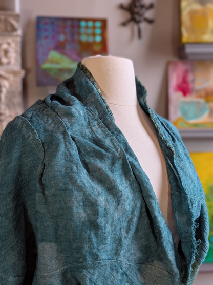 Teal textured garment on a mannequin with colorful abstract paintings in the background