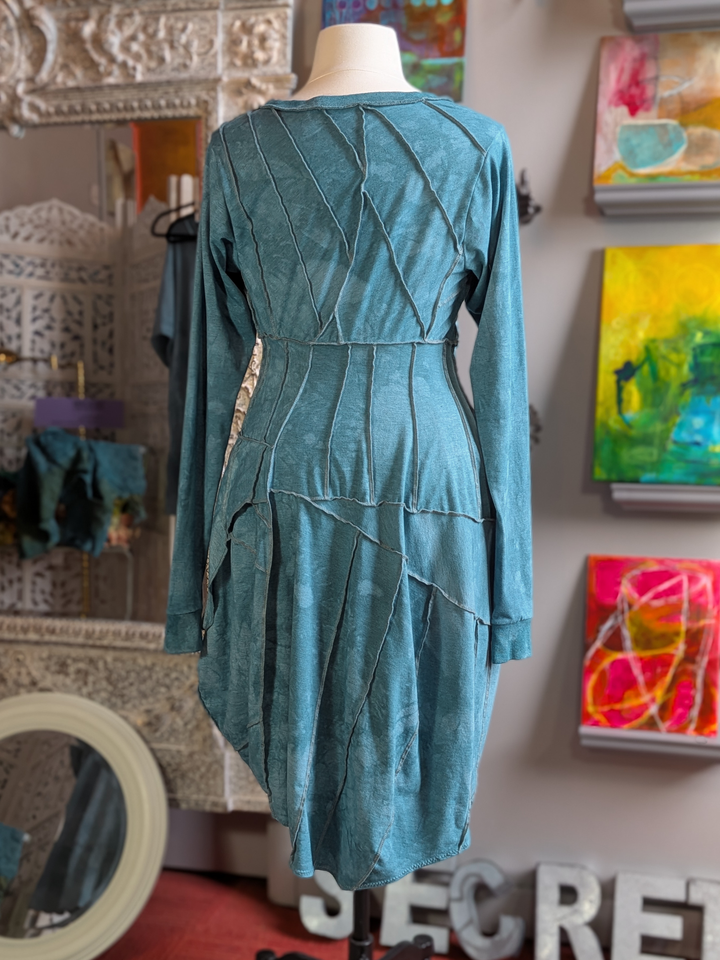 Teal dress on a mannequin in a room with colorful artwork on the wall.