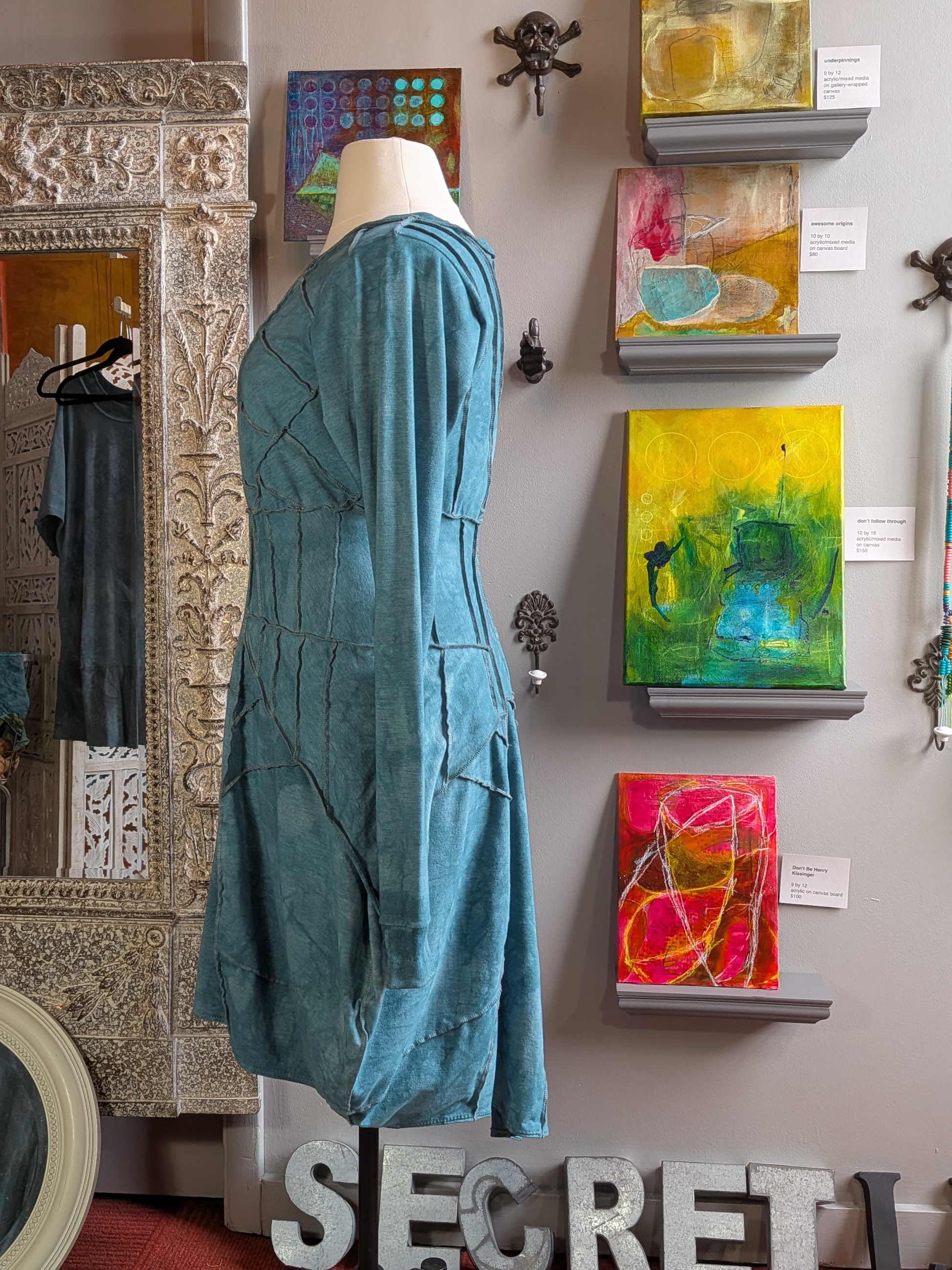 Teal dress on a mannequin in front of wall art in an art gallery.