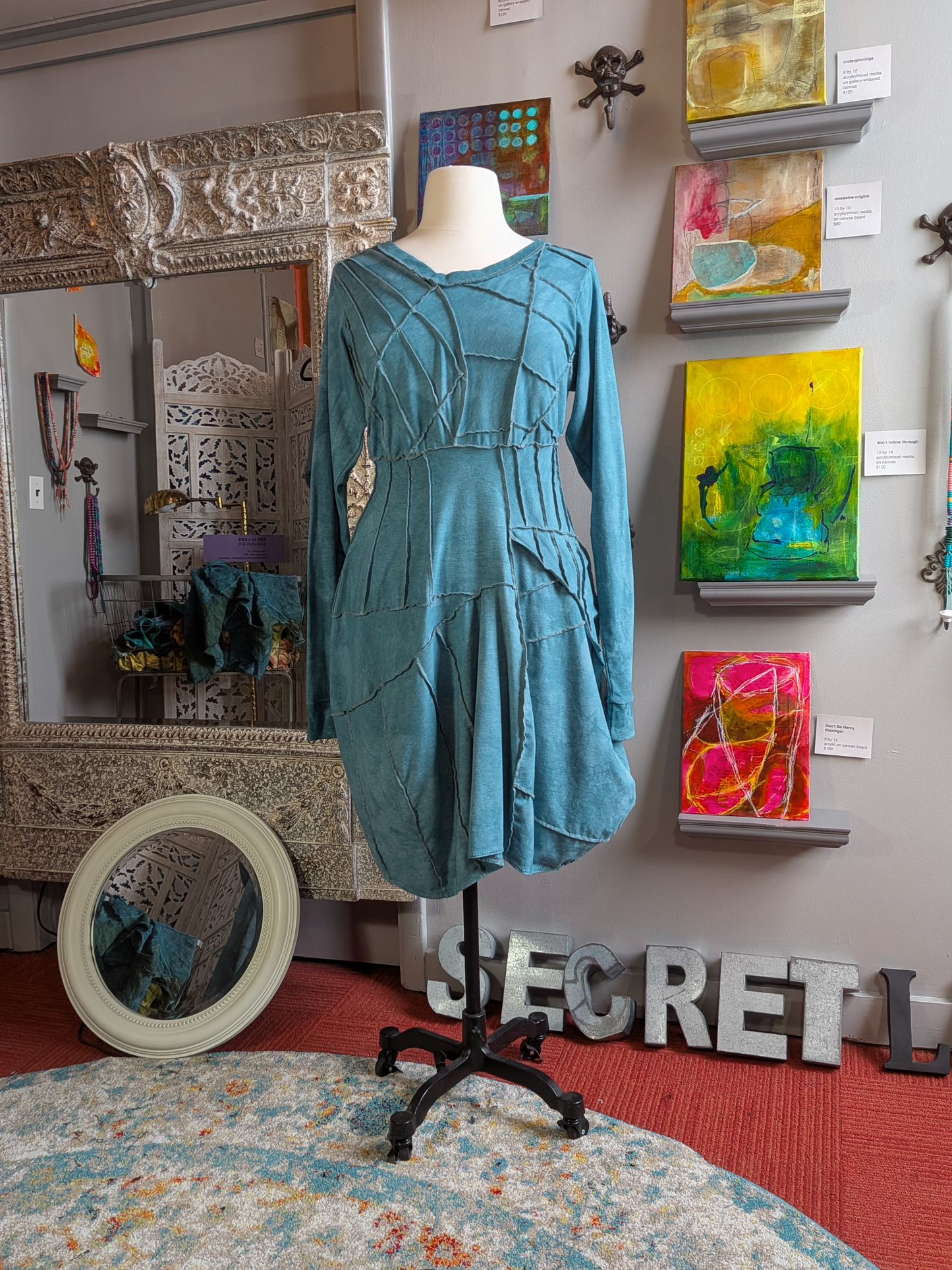Teal dress on a mannequin in front of wall art and decorative items.